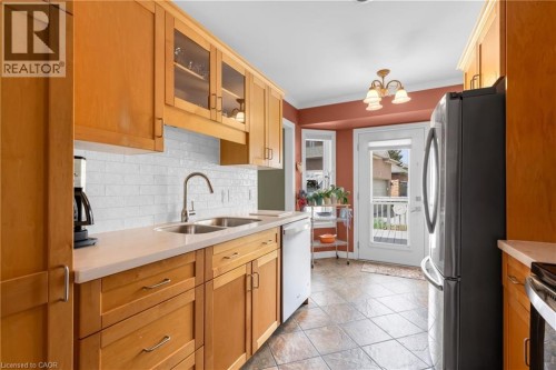 Kitchen featuring wood cabinetry, light-toned countertops, a white subway tile backsplash, a stainless steel double basin sink with a gooseneck faucet, and ceramic tile flooring - 50 Spadara Drive, Hamilton, ON - Indoor Photo Showing Kitchen With Double Sink