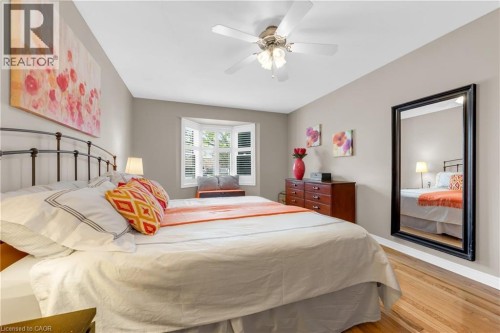 Recessed bay window with plantation shutters, ceiling fan, warm wood-finish flooring, and neutral wall tones - 50 Spadara Drive, Hamilton, ON - Indoor Photo Showing Bedroom