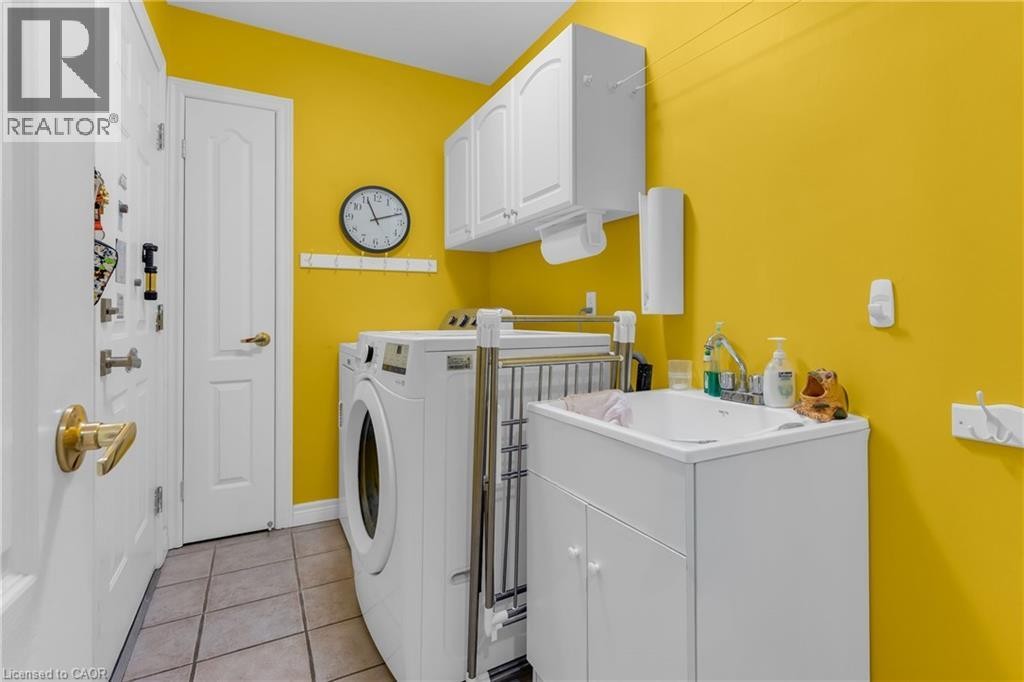 Laundry area featuring tile flooring, white cabinetry, a utility sink with a built-in cabinet, and a wall-mounted paper towel dispenser - 50 Spadara Drive, Hamilton, ON - Indoor Photo Showing Laundry Room