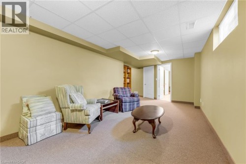 Carpeted lower-level room featuring drop ceiling, recessed wall sections, and a built-in bookshelf - 50 Spadara Drive, Hamilton, ON - Indoor
