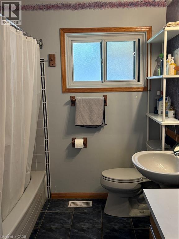 Bathroom featuring a white bathtub with tiled surround, a toilet, and a sink with a white counter - 82 Blackwood Crescent, Hamilton, ON