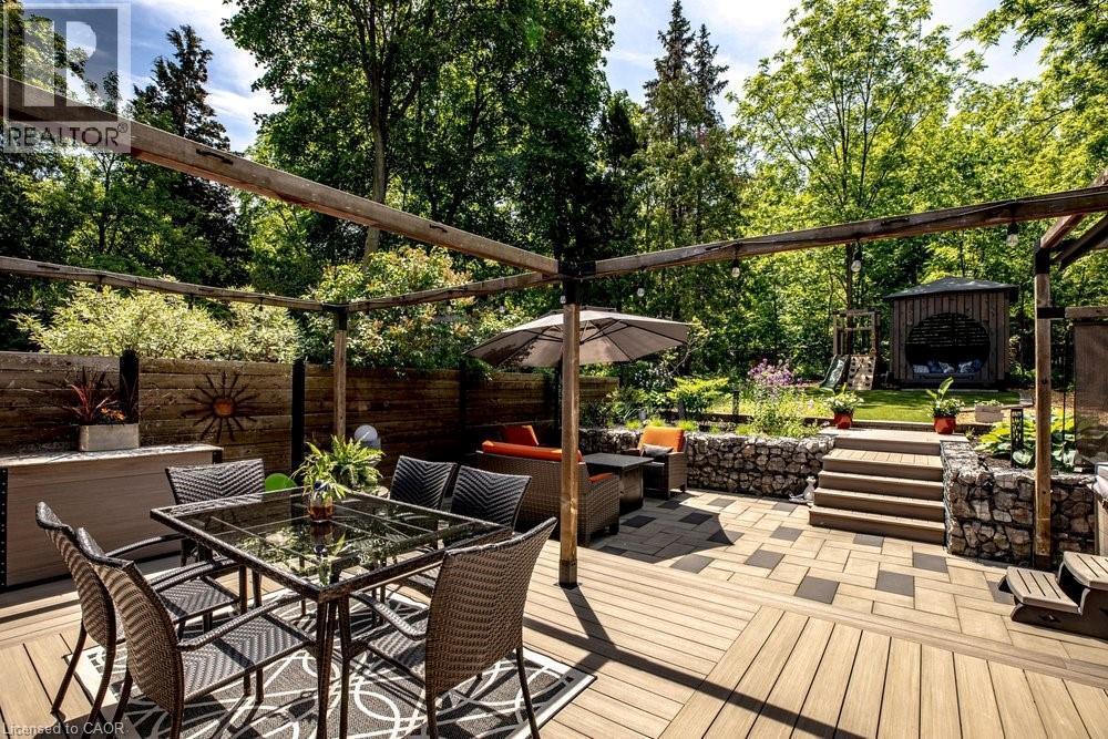 Multi-level outdoor living space featuring a wood-finish deck, stone retaining walls, and a separate paved patio area - 99 Hillcrest Avenue, Hamilton, ON - Outdoor