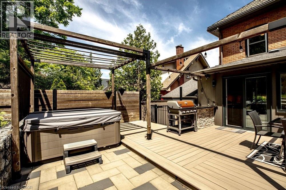 Outdoor living space featuring a wood-finish pergola, a built-in spa, composite decking, a paver patio, and sliding glass door access to the interior - 99 Hillcrest Avenue, Hamilton, ON - Outdoor With Deck Patio Veranda With Exterior