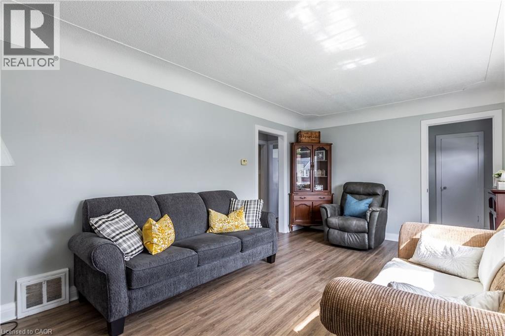 Living area featuring wood-finish flooring, light gray wall paint, white trim, and a textured white ceiling - 20 West 1St Street, Hamilton, ON