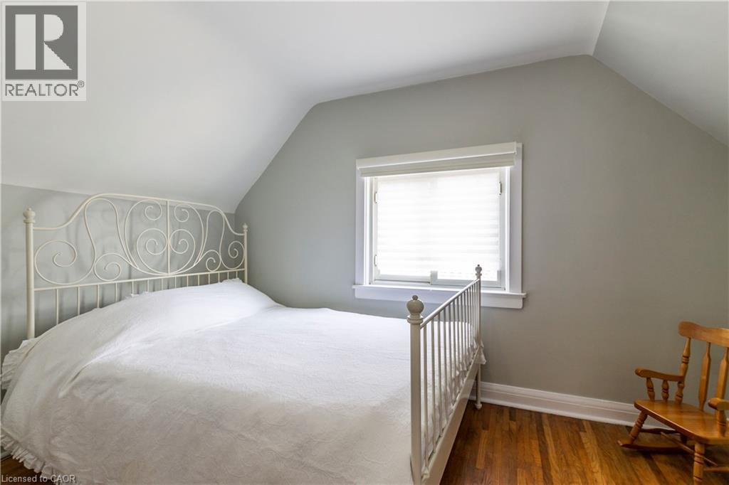 Interior room featuring hardwood flooring, a window with blinds, light gray walls, white trim, and an angled ceiling - 20 West 1St Street, Hamilton, ON