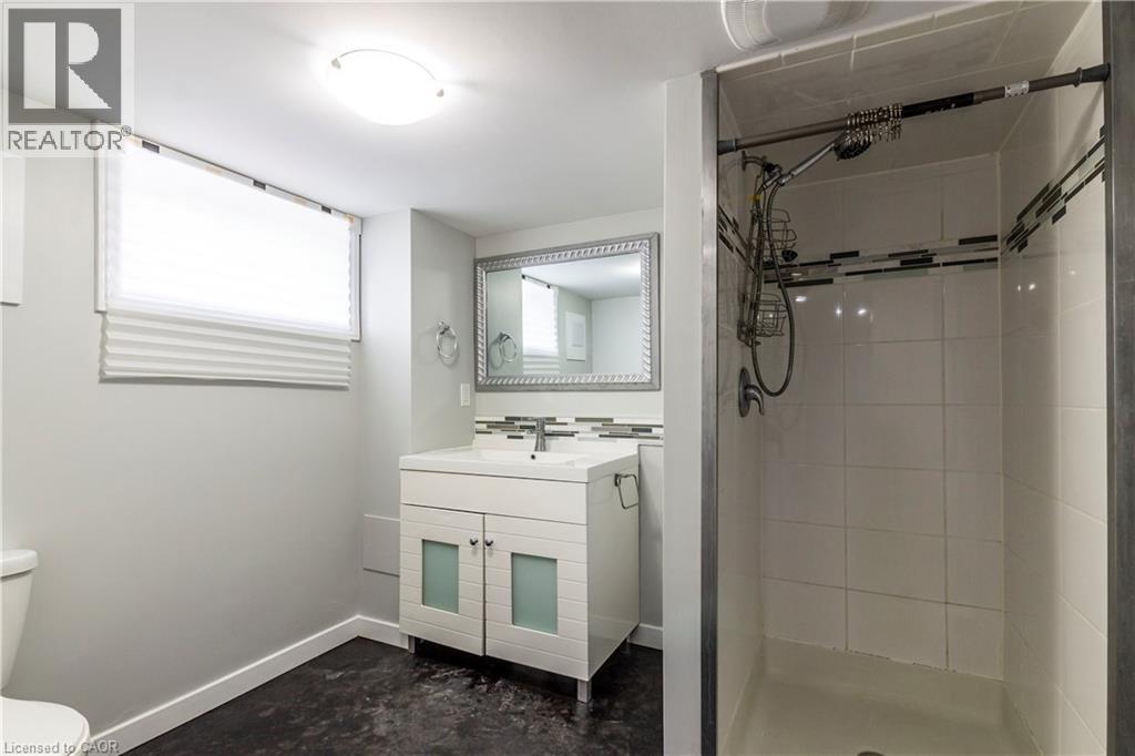 Full bathroom featuring a walk-in shower with tile surround, a white vanity with frosted glass cabinet doors, a rectangular undermount sink, and a framed vanity mirror - 20 West 1St Street, Hamilton, ON