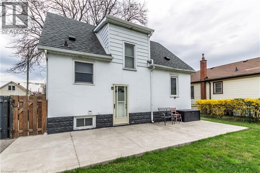 Rear exterior showcasing a concrete patio, expansive green lawn, and a light-colored stucco finish with a dark stone veneer foundation - 20 West 1St Street, Hamilton, ON