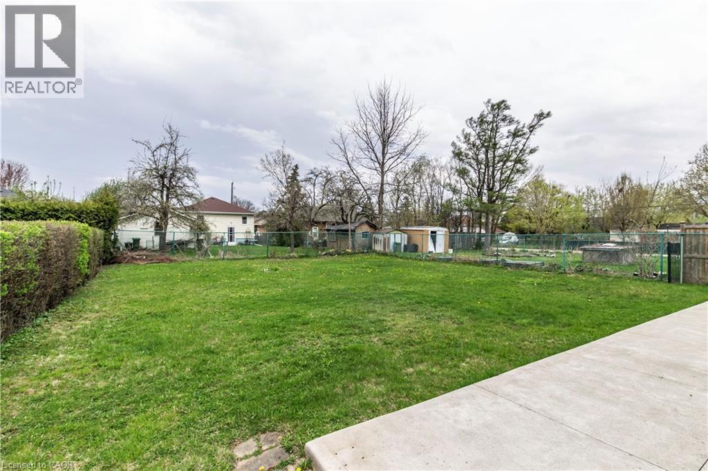 Expansive backyard space featuring a large lawn area, mature trees, and a concrete patio - 20 West 1St Street, Hamilton, ON