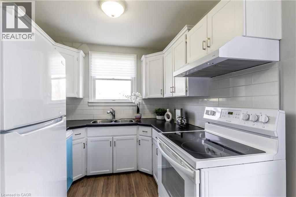 Well-appointed kitchen featuring white cabinetry, black countertops, white subway tile backsplash, stainless steel double basin sink, and wood-finish flooring - 20 West 1St Street, Hamilton, ON