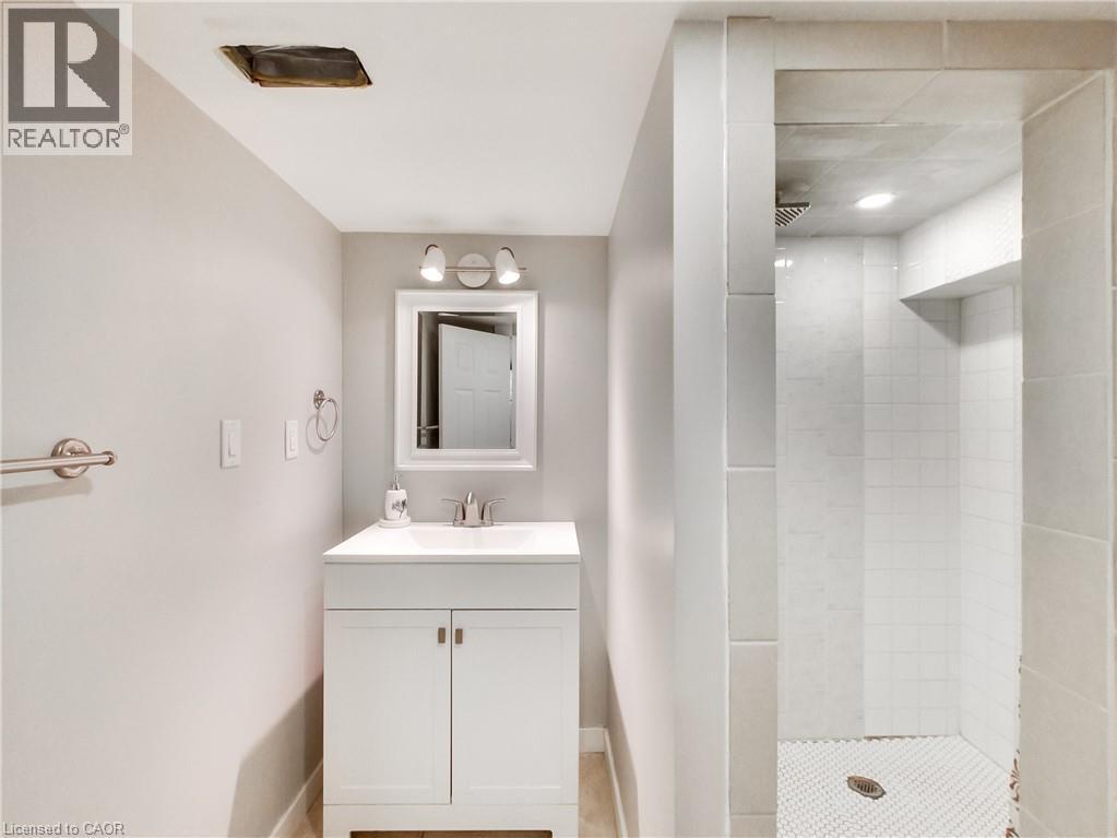 Bathroom featuring a white vanity with integrated sink, chrome faucet, and rectangular mirror with task lighting - 229 Parkdale Avenue N, Hamilton, ON