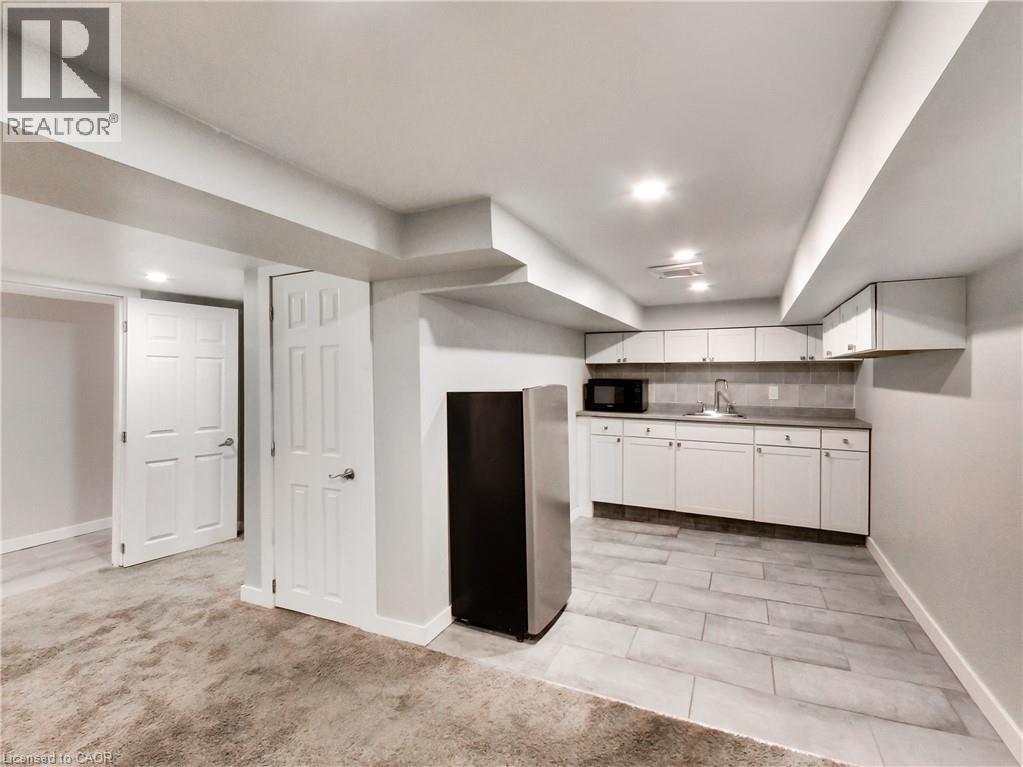 Lower-level kitchenette featuring white cabinetry, a stainless steel refrigerator, and a tile backsplash - 229 Parkdale Avenue N, Hamilton, ON