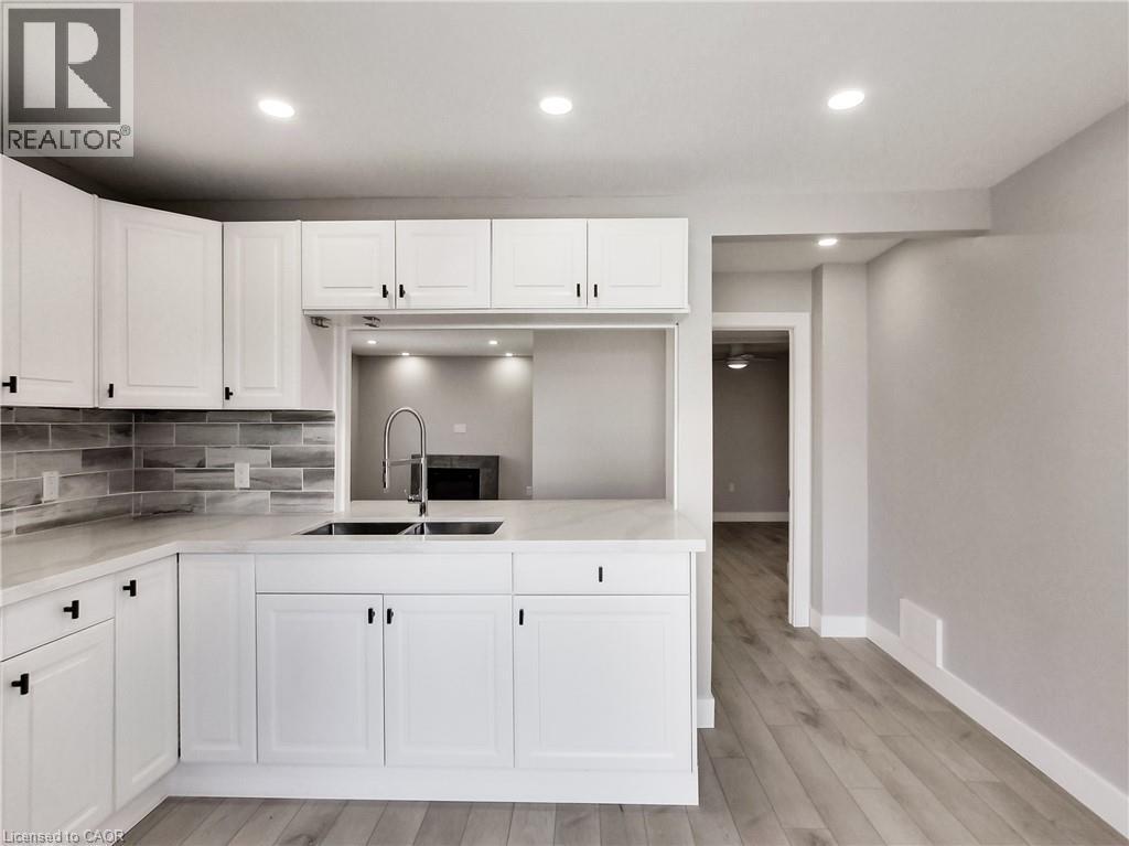 Kitchen featuring white shaker-style cabinetry, a stainless steel double basin sink with a gooseneck faucet, light-toned countertops, and a gray subway tile backsplash - 229 Parkdale Avenue N, Hamilton, ON
