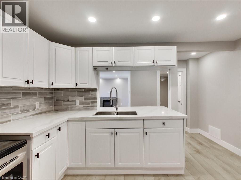 Contemporary kitchen featuring white cabinetry with black hardware, white countertops, a mosaic tile backsplash, and light wood-finish flooring - 229 Parkdale Avenue N, Hamilton, ON