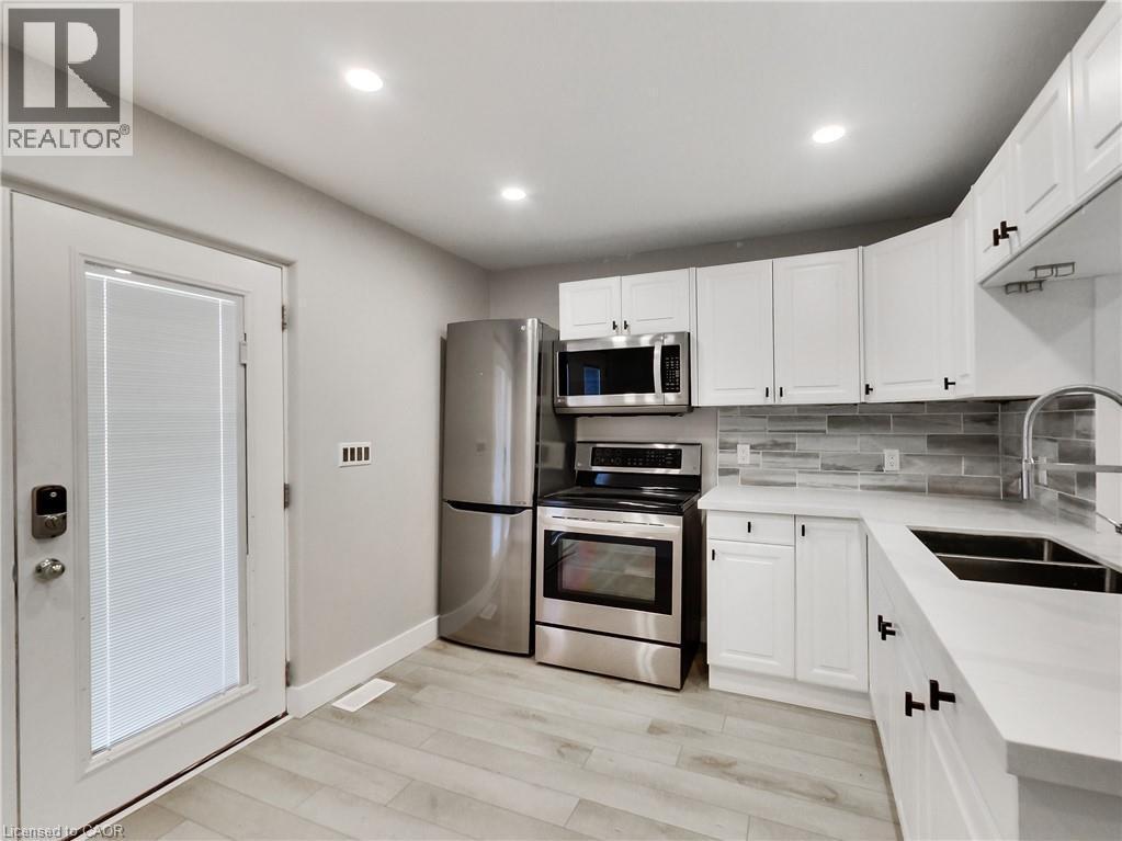 Modern kitchen featuring white shaker cabinetry, stainless steel appliances, light wood-finish flooring, a contemporary tile backsplash, and recessed lighting - 229 Parkdale Avenue N, Hamilton, ON