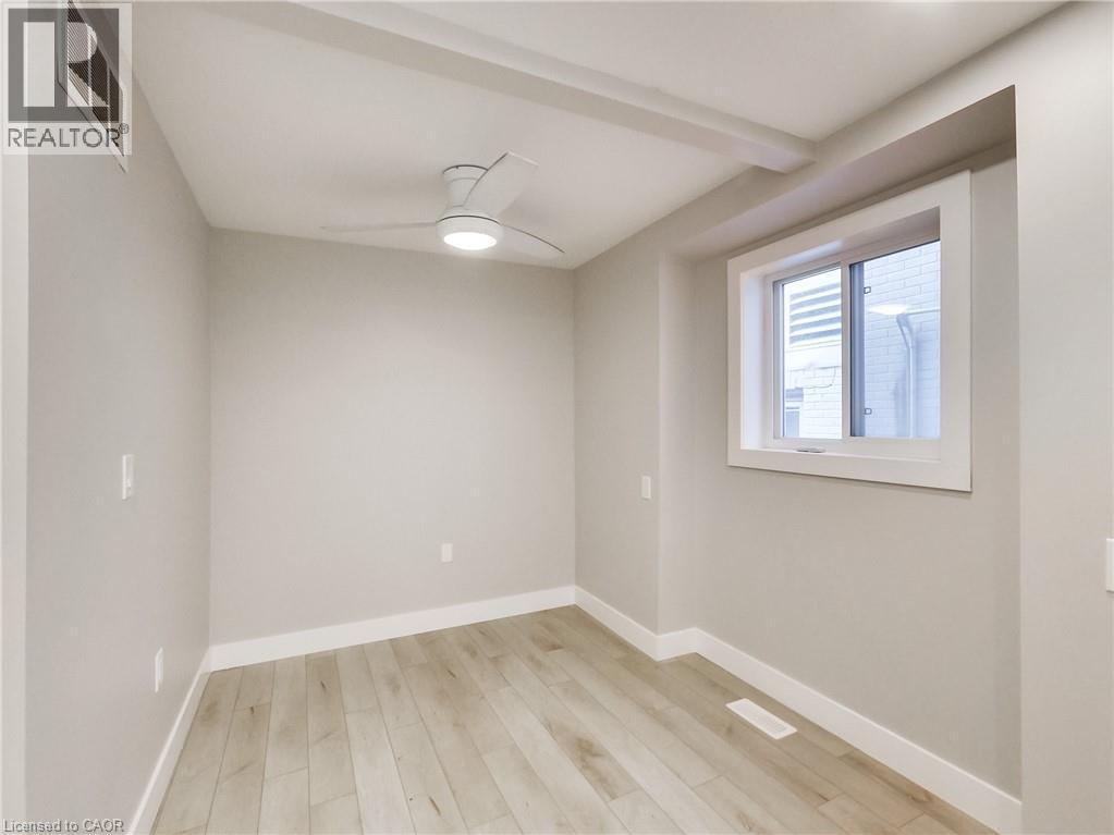 Room featuring light wood-finish flooring, a modern ceiling fan with integrated lighting, a recessed window, and neutral-toned walls with white trim - 229 Parkdale Avenue N, Hamilton, ON