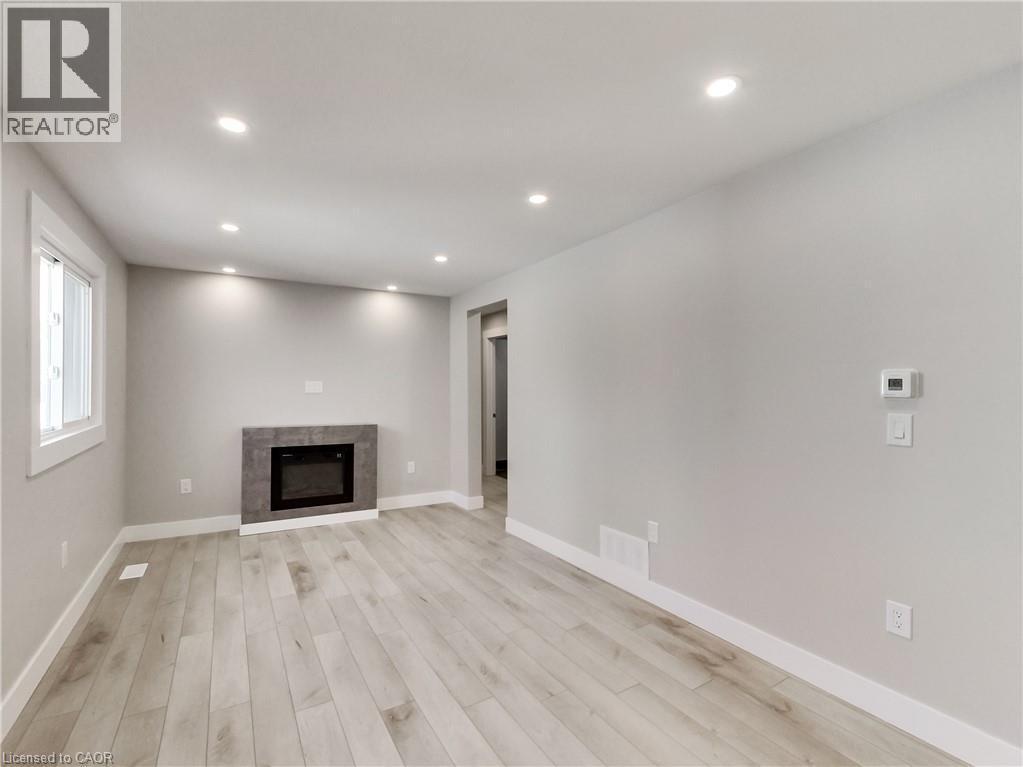 Spacious room featuring light wood-finish flooring, recessed lighting, and a modern fireplace with a tiled surround - 229 Parkdale Avenue N, Hamilton, ON