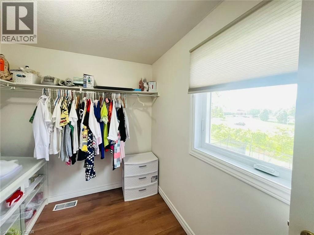 Spacious walk-in closet featuring wood-finish flooring, a single window with a privacy shade, and built-in shelving with hanging rods - 136 Hidden Creek Drive, Kitchener, ON