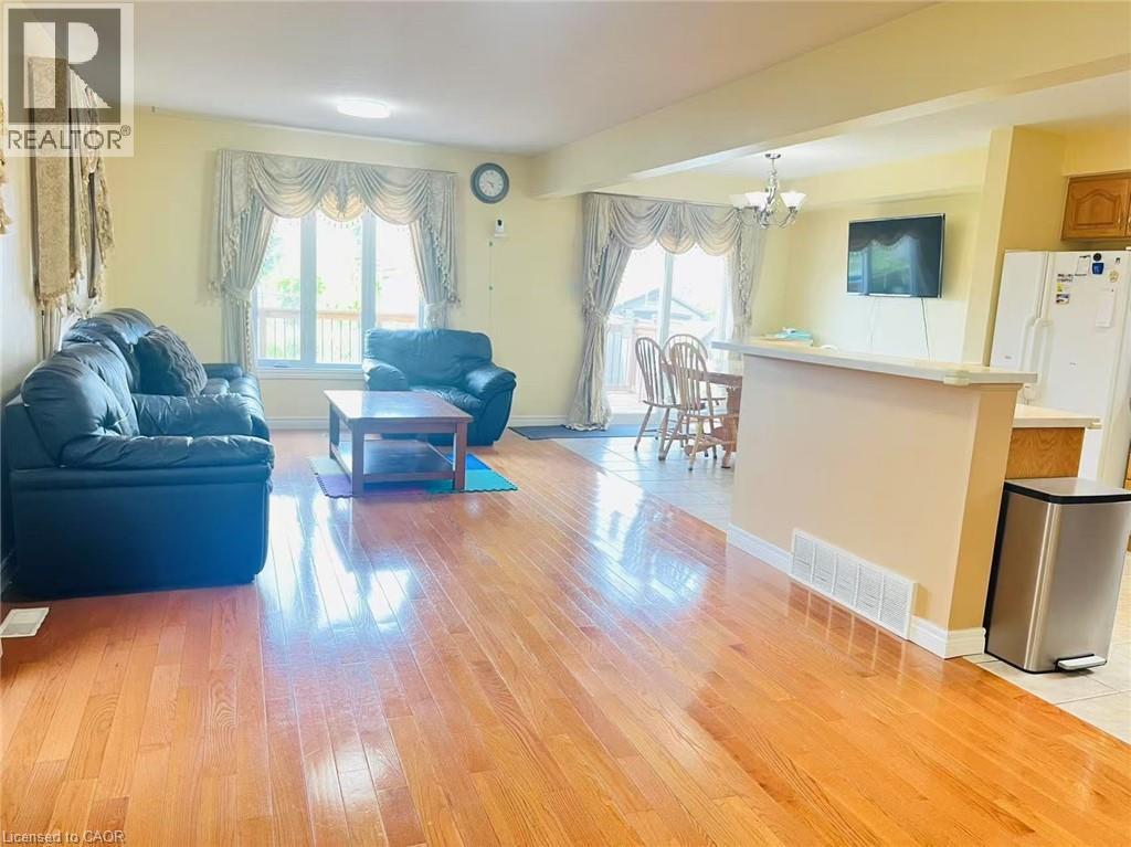 Open-concept living area featuring wood-finish flooring, a large window, and a dining area with a chandelier - 136 Hidden Creek Drive, Kitchener, ON