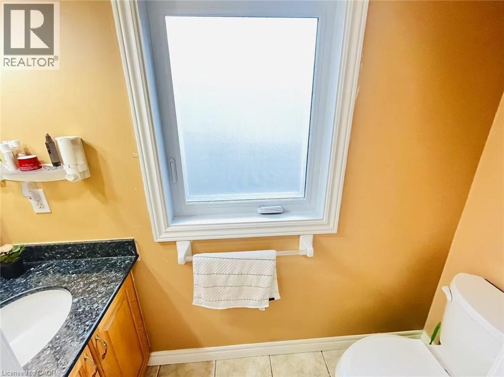 Bathroom featuring a frosted window with white trim, a toilet, and a vanity with a dark speckled countertop and an undermount sink - 136 Hidden Creek Drive, Kitchener, ON
