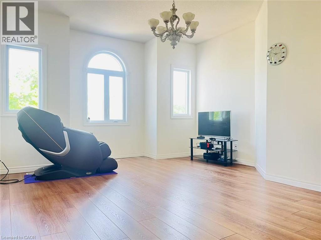Spacious room featuring wood-finish flooring, white walls, and a multi-light chandelier - 136 Hidden Creek Drive, Kitchener, ON