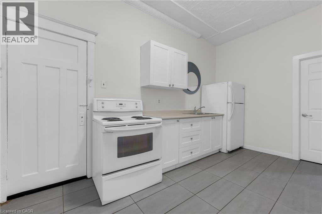 Kitchen area featuring a white electric range, white cabinetry, a single basin sink, and a white refrigerator - 1371 Main Street E, Hamilton, ON - Indoor Photo Showing Kitchen