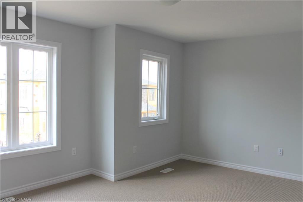 Neutral-toned interior with two windows featuring white trim, complementing light gray walls, and textured carpet flooring - 124 Compass Trail Unit# 14, Cambridge, ON
