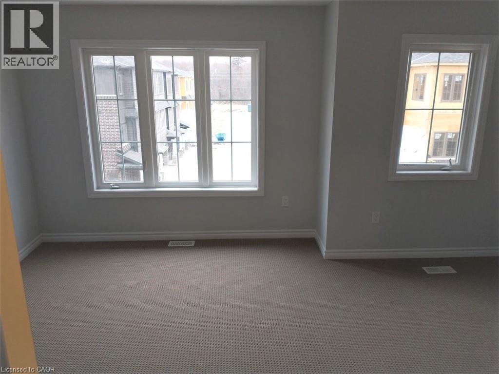 Spacious room featuring multiple windows with white trim, light gray painted walls, and neutral-toned carpeting - 124 Compass Trail Unit# 14, Cambridge, ON