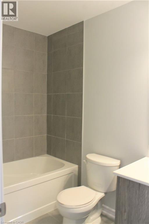 Bathroom featuring a white bathtub, grey wall tiling, a white toilet, and a vanity with a light-colored countertop - 124 Compass Trail Unit# 14, Cambridge, ON