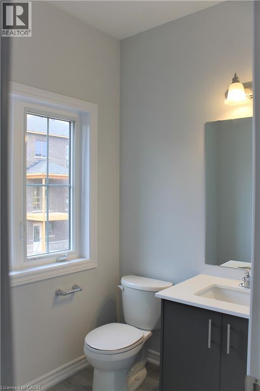 Bathroom featuring a single window, white trim, a toilet, a vanity with a white countertop and dark cabinetry, and a wall-mounted light fixture - 124 Compass Trail Unit# 14, Cambridge, ON