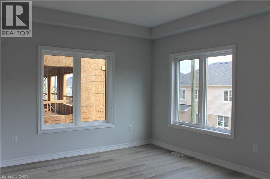 Spacious room featuring two large windows with white trim, light gray painted walls, a tray ceiling, and wood-finish flooring - 124 Compass Trail Unit# 14, Cambridge, ON