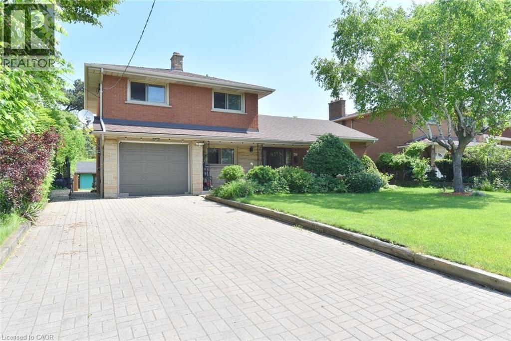 Brick and stone facade residence featuring a two-car garage, extensive paver driveway, and a mature front yard with established landscaping - 372 Fennell Avenue W, Hamilton, ON