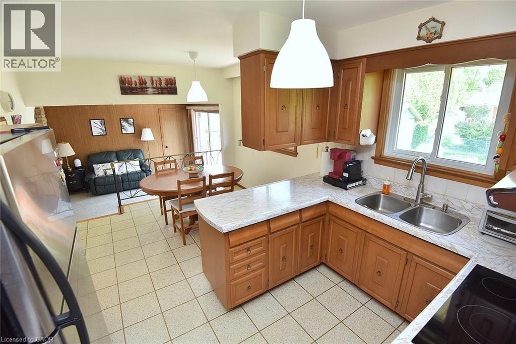 Kitchen featuring wood cabinetry, white countertop surfaces, and a double basin stainless steel sink with a gooseneck faucet - 372 Fennell Avenue W, Hamilton, ON