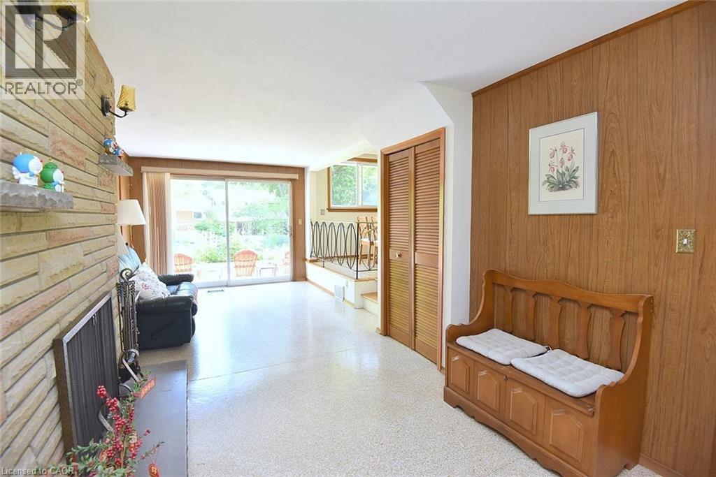 Spacious living area featuring a stone fireplace, wood-finish wall paneling, light terrazzo flooring, and sliding glass doors to the exterior - 372 Fennell Avenue W, Hamilton, ON
