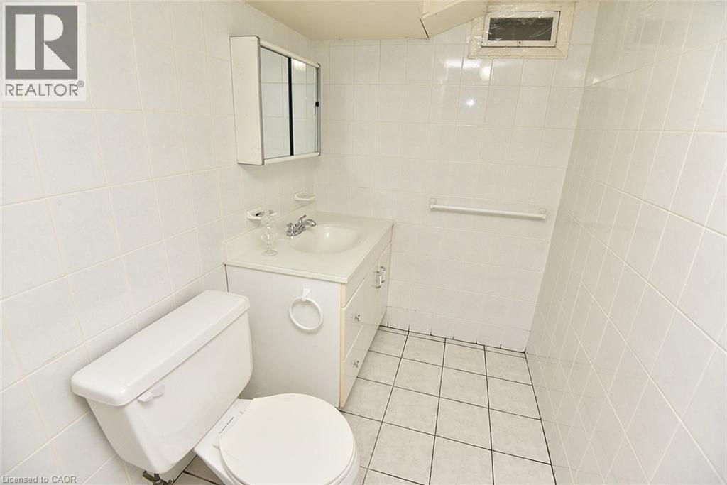 White tiled bathroom featuring a vanity with a drop-in sink, wall-mounted medicine cabinet, white toilet, and tiled flooring - 372 Fennell Avenue W, Hamilton, ON