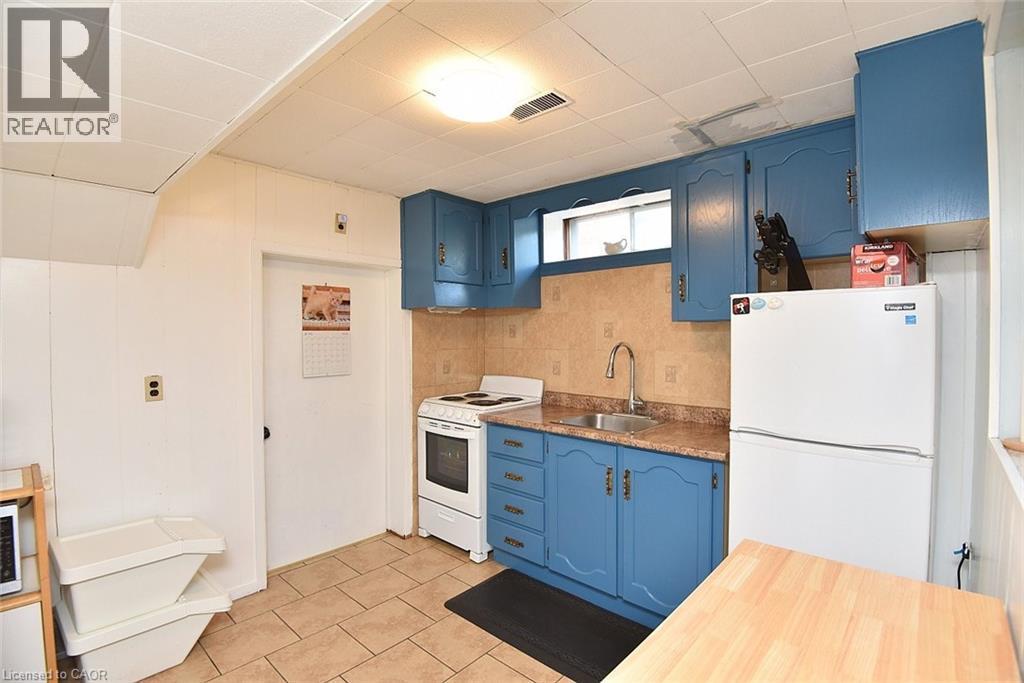 Kitchen featuring blue cabinetry, a stainless steel sink with a high-arc faucet, a brown tiled backsplash, and light-toned tile flooring - 372 Fennell Avenue W, Hamilton, ON