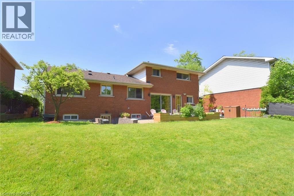 Spacious rear lawn with a brick exterior, a large wooden deck, sliding glass doors, and mature landscaping - 372 Fennell Avenue W, Hamilton, ON
