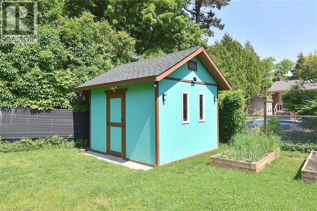 Turquoise shed with brown trim, featuring a shingled roof, two side windows, and wall-mounted exterior lighting - 372 Fennell Avenue W, Hamilton, ON