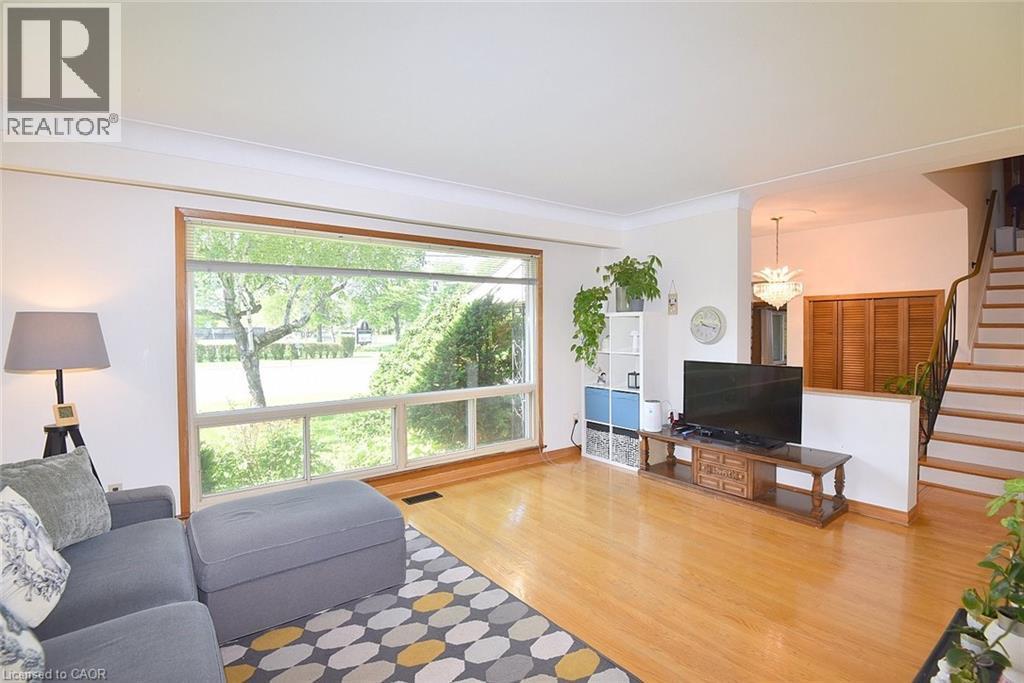 Living area featuring expansive picture windows, wood-finish flooring, white wall tones, and a staircase with a dark metal handrail - 372 Fennell Avenue W, Hamilton, ON