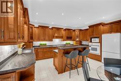 Expansive kitchen featuring custom wood cabinetry, granite countertops, white tile backsplash, a central island with bar seating, and integrated appliances -