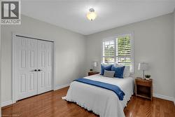 Room featuring wood-finish flooring, a double window with plantation shutters, ceiling-mounted lighting, and a bi-fold closet -