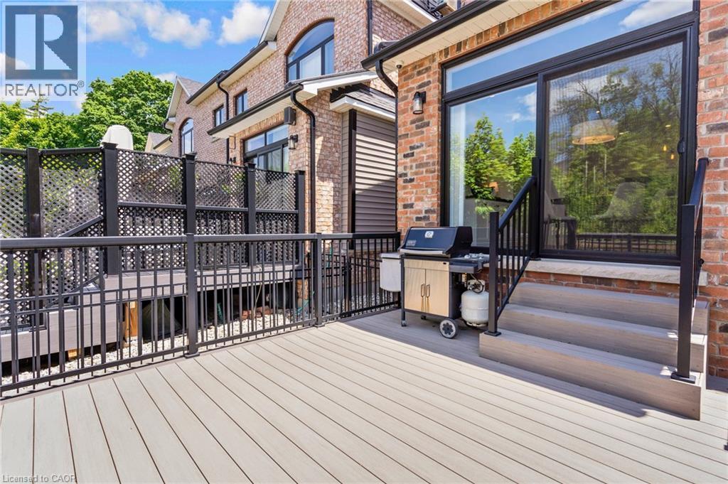 Spacious composite deck featuring a black metal railing, lattice privacy screen, exterior wall sconce, and a sliding glass door for outdoor access - 12 George Street, Waterloo, ON