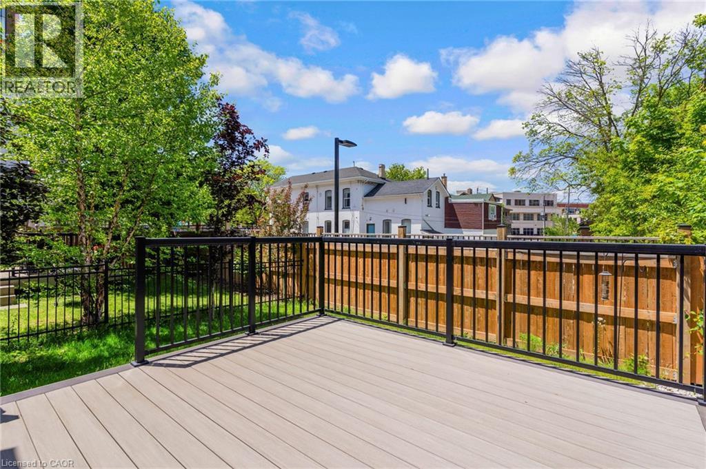 Outdoor composite decking with black metal railings, bordered by a wooden privacy fence and a wrought iron fence - 12 George Street, Waterloo, ON