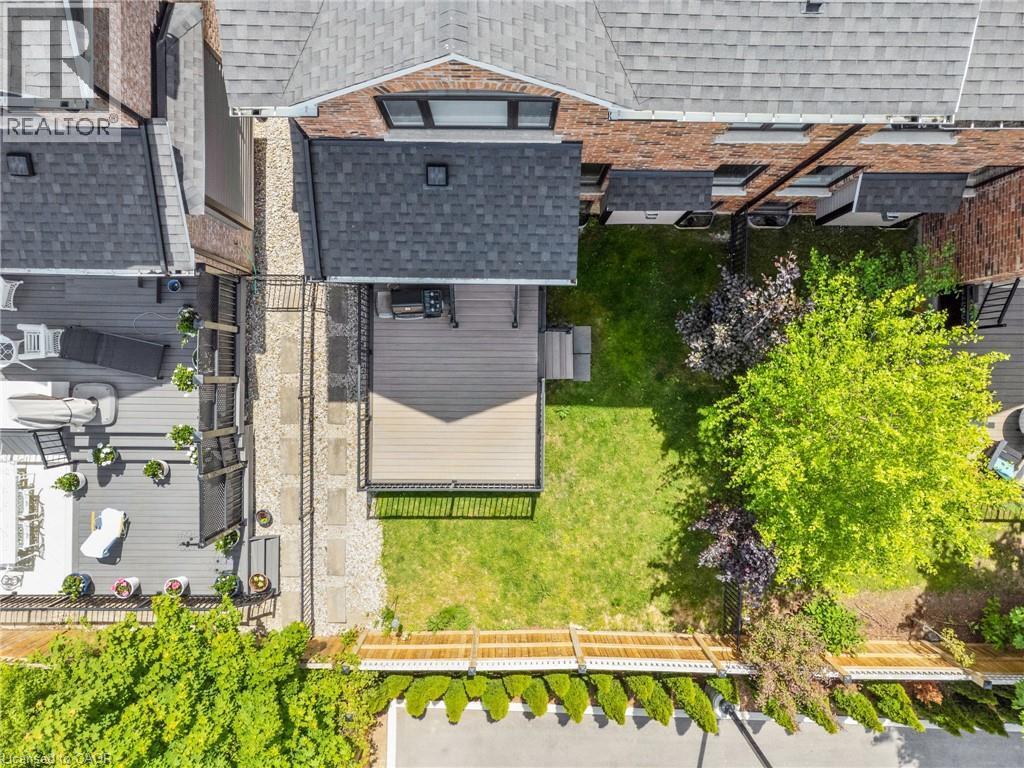 Manicured backyard featuring a spacious deck with dark railing, a verdant lawn, mature trees, and a privacy fence - 12 George Street, Waterloo, ON