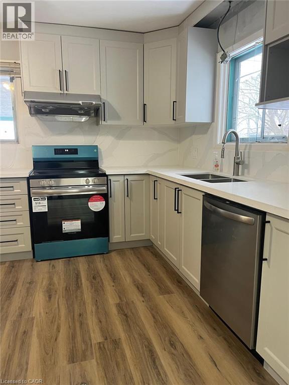 Modern kitchen featuring light-toned cabinetry with dark hardware, wood-finish flooring, stainless steel appliances, a double basin sink with a high-arc faucet, and white countertops - 102 Massey Avenue, Kitchener, ON