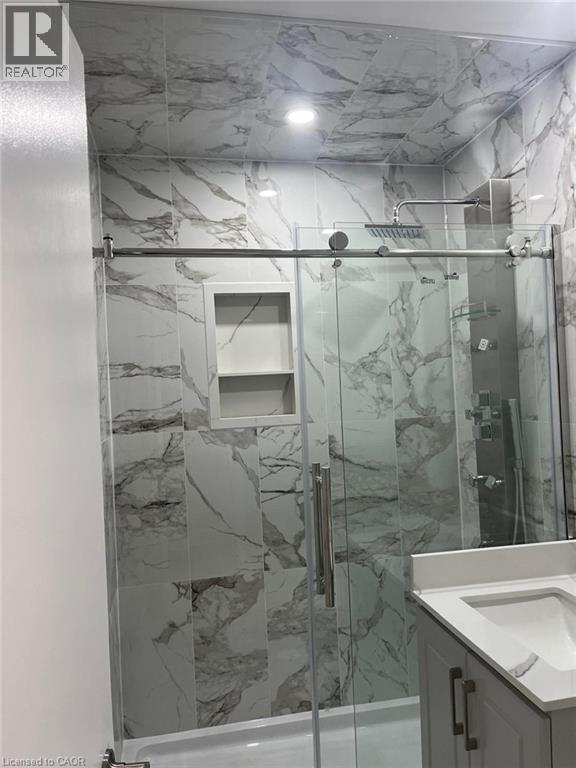 Enclosed shower with sliding glass doors, white tiled walls with grey veining, a built-in shower niche, and a rainfall showerhead - 102 Massey Avenue, Kitchener, ON