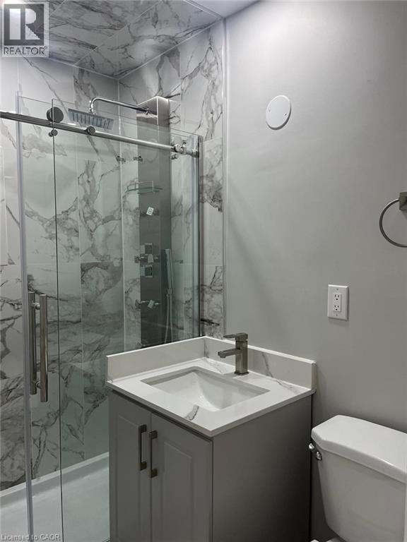 Bathroom featuring a walk-in shower with clear glass enclosure, marble-patterned wall tiles, and a rainfall shower head - 102 Massey Avenue, Kitchener, ON