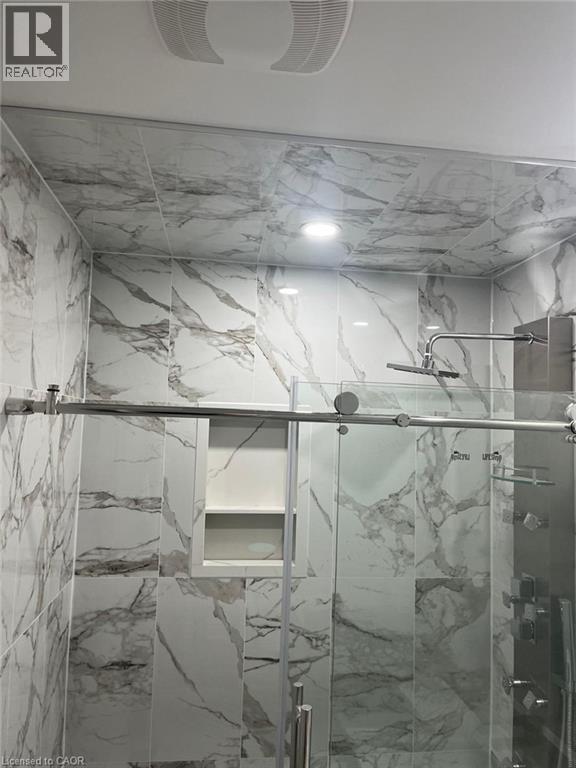 Shower enclosure featuring marble-look wall tiling, recessed lighting, a built-in shower niche, and a sliding glass door with a stainless steel bar handle - 102 Massey Avenue, Kitchener, ON