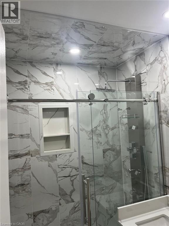 Shower enclosure featuring full-height marble-look tile, a built-in shower niche, and a rain shower head with a multi-function panel - 102 Massey Avenue, Kitchener, ON