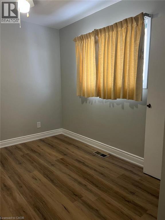 Room featuring wood-finish flooring, light grey walls, white baseboards, and a window with curtains - 102 Massey Avenue, Kitchener, ON