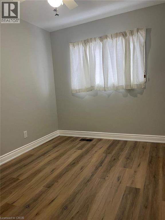 Interior space featuring wood-finish flooring, light grey walls, white baseboards, and a window with sheer white curtains - 102 Massey Avenue, Kitchener, ON